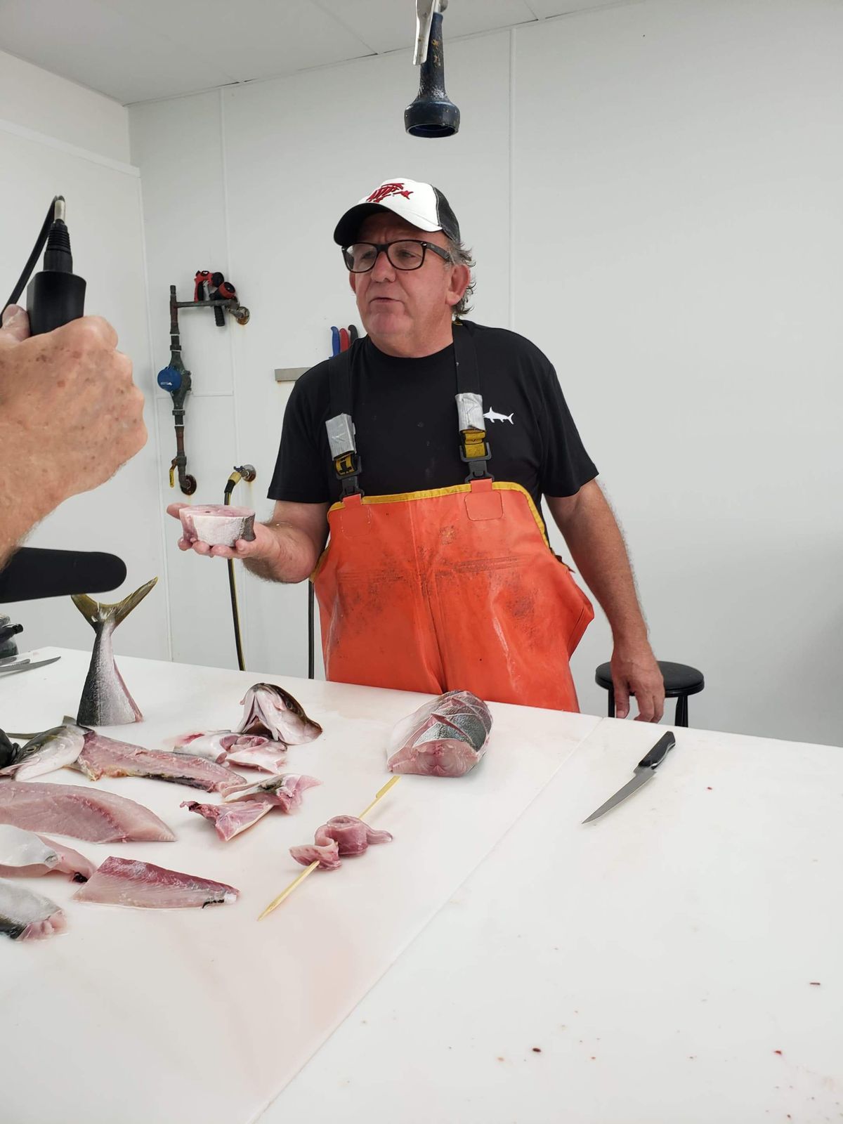 Fishmonger Tommy Gomes wearing overalls while talking and filleting fish