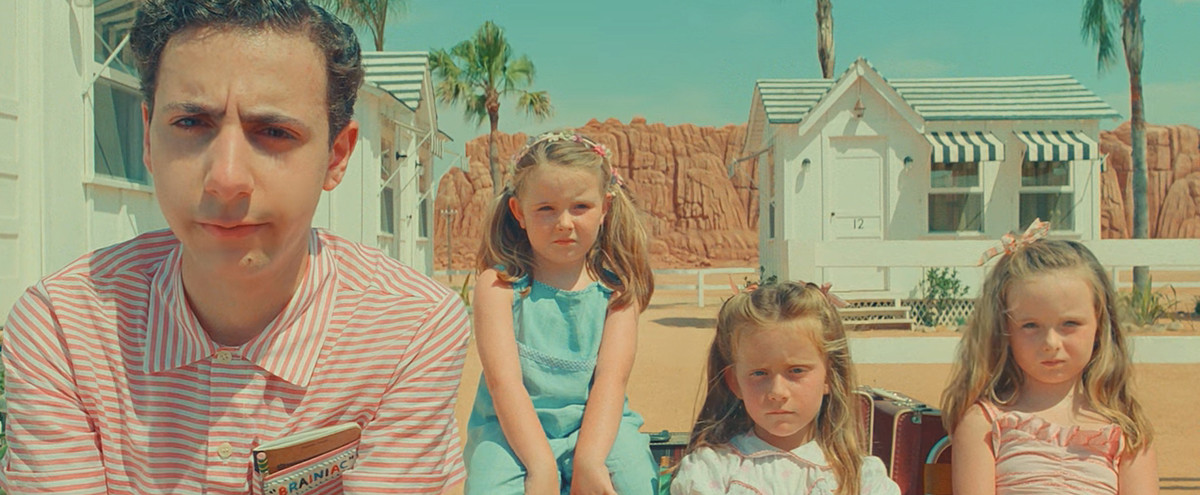 Teenage boy Woodrow Steenbeck (Jake Ryan) and his triplets, three young girls, sit arrayed in front of a pale-white desert motel in Wes Anderson's Asteroid City