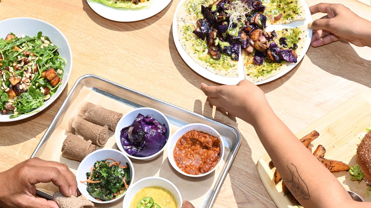 Hands pull apart dishes from a new sunny Ethiopian restaurant’s wooden table.