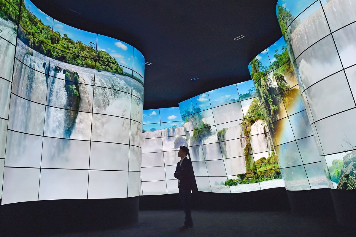 A person stands looking at walls that are a giant curved screen showing a waterfall landscape.