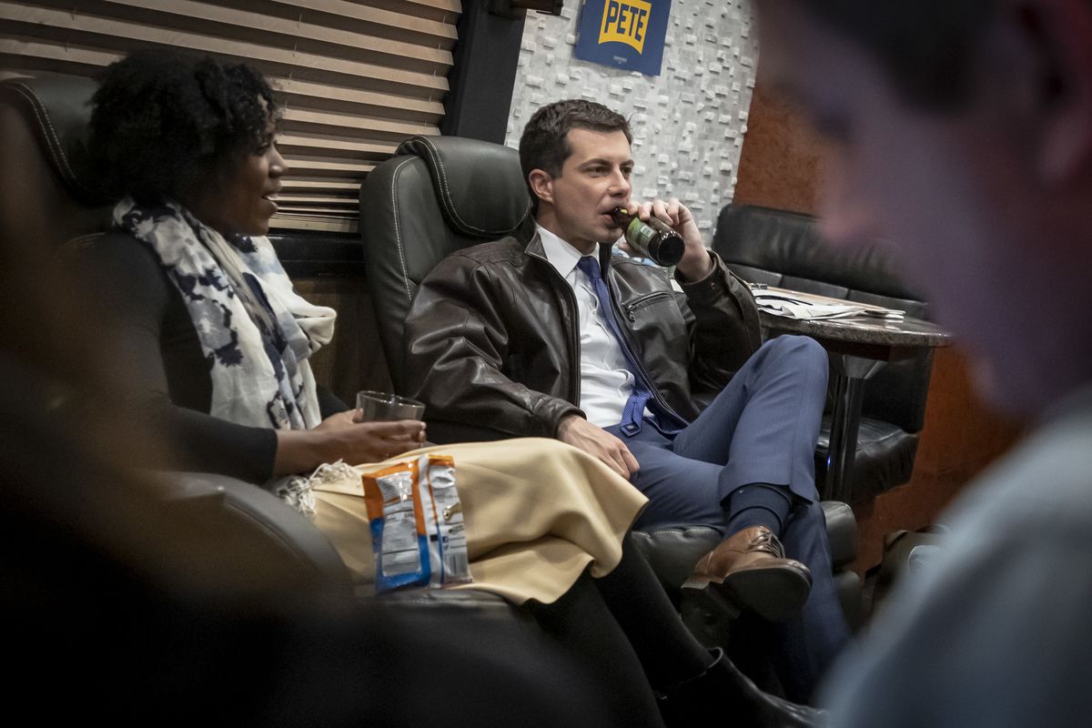 Buttigieg drinks a beer while sitting in a chair.