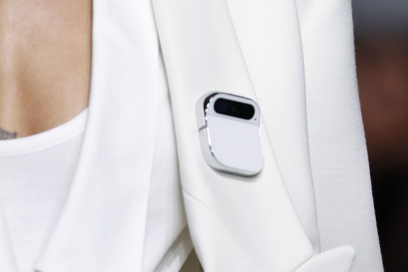 Close-up shot of a white Ai Pin on a grayish white jacket lapel.