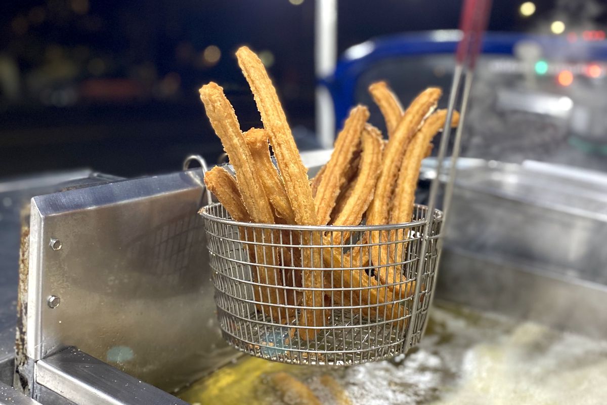 A wire basket hanging above hot oil filled with golden rods of freshly fried churros at Churros El Bochito.