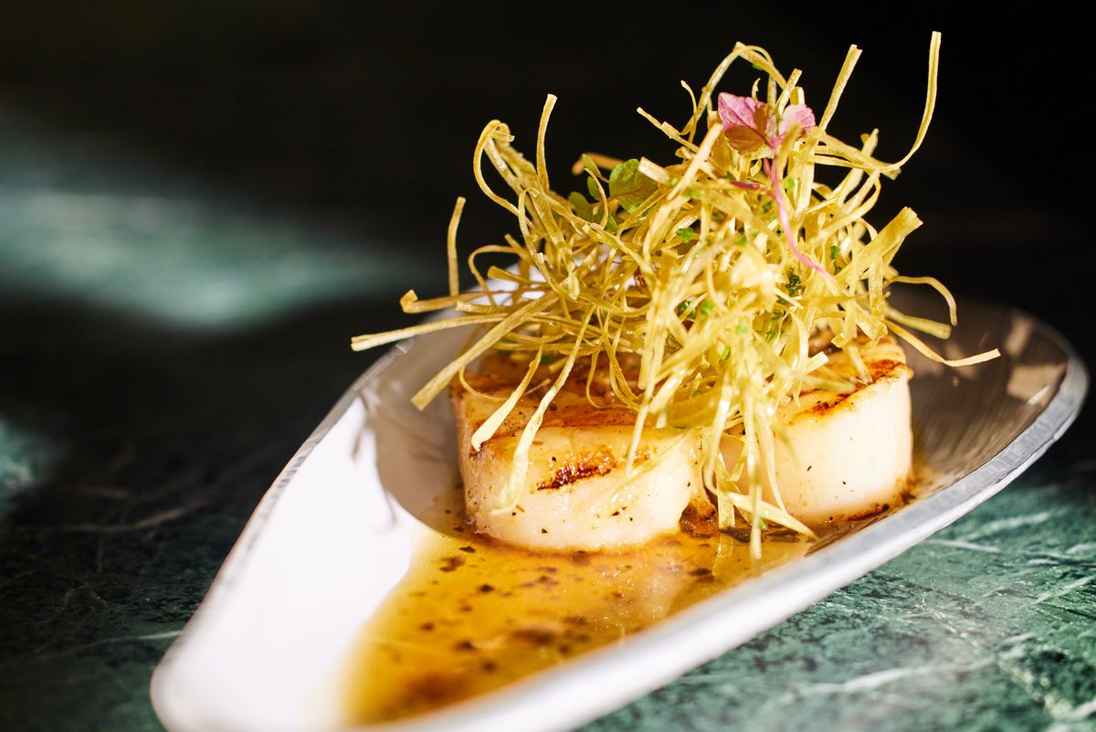 Seared scallops garnished with chive strips and set in a yellow broth.