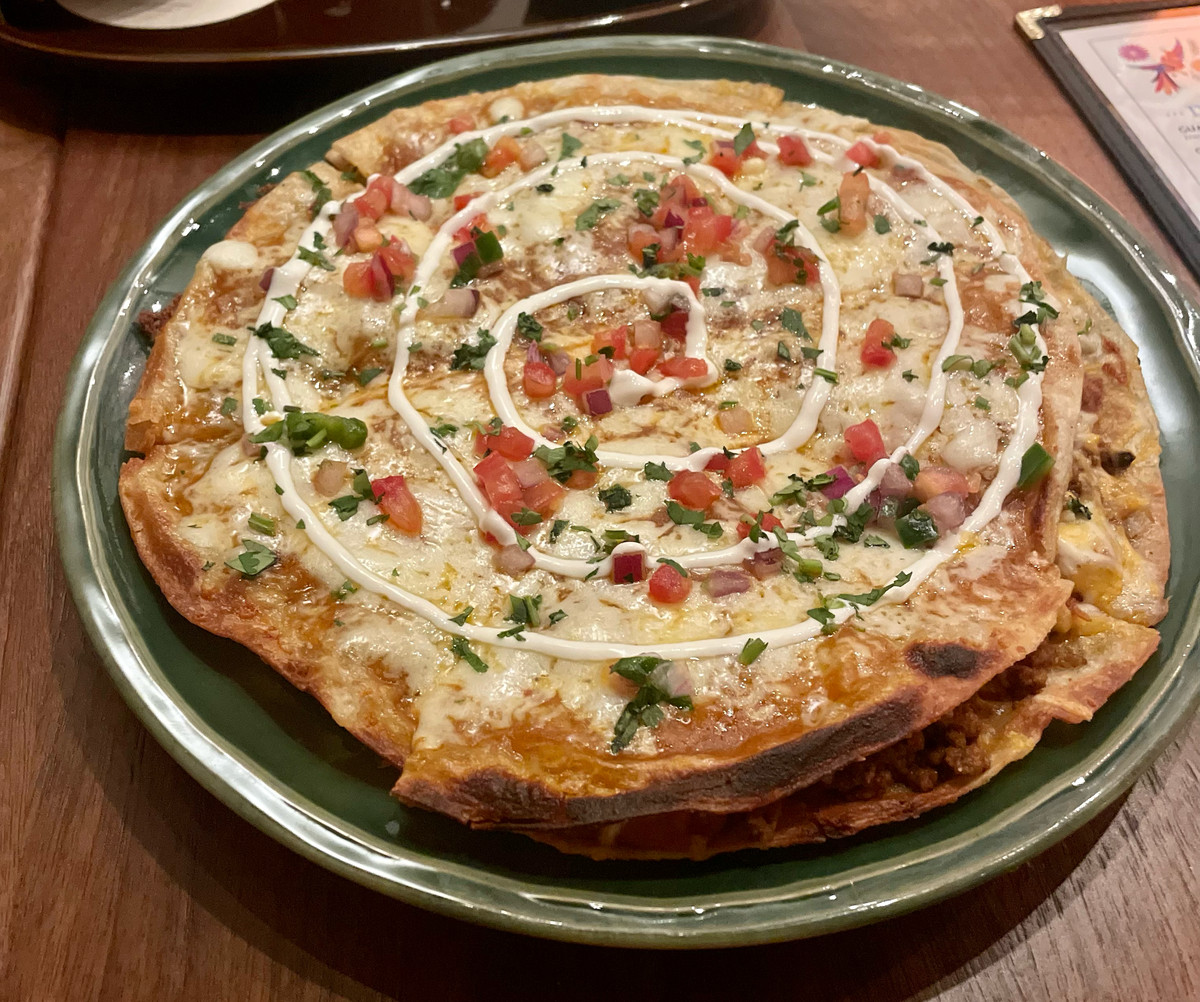 A Tex-Mex pizza sits on a circular plate, and has rounds of sour cream circling the top.
