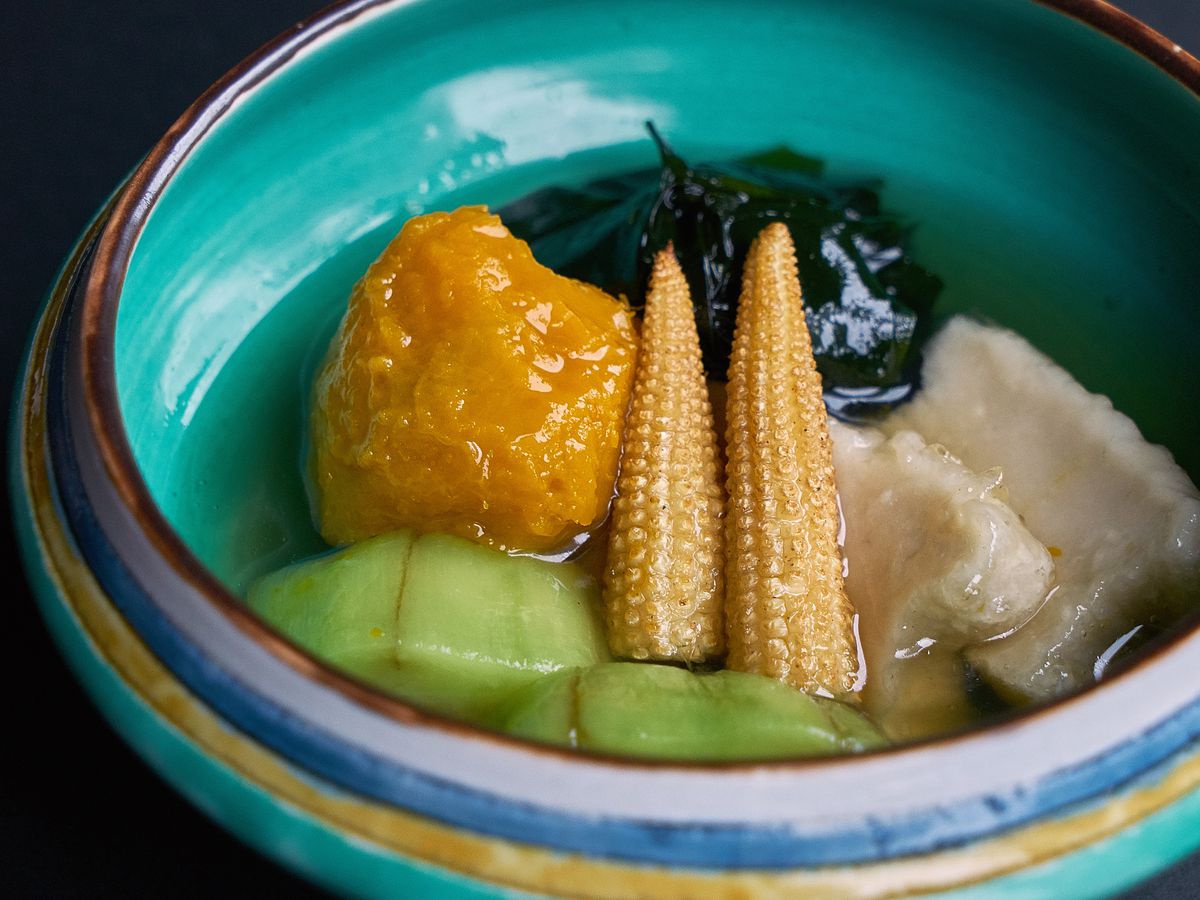 A bright blue ceramic bowl of various cooked vegetables in broth.