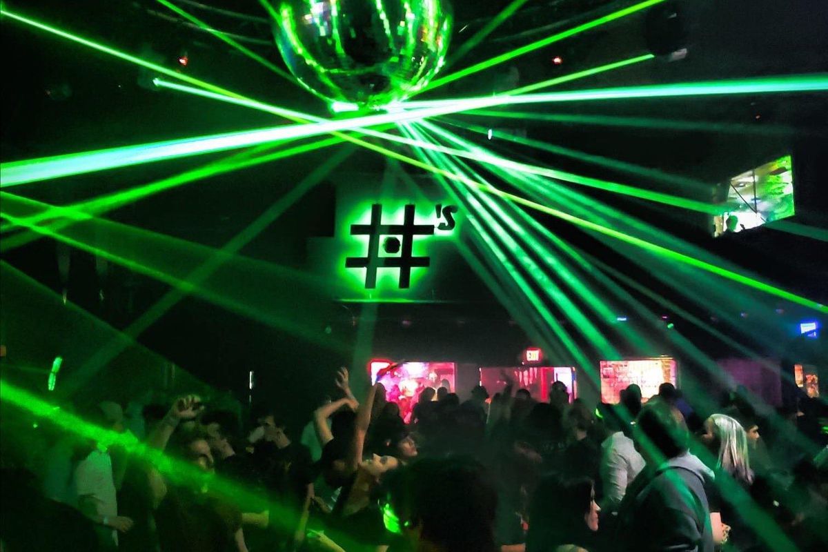a nightclub lit with neon green lasers with a disco ball above a dancing crowd