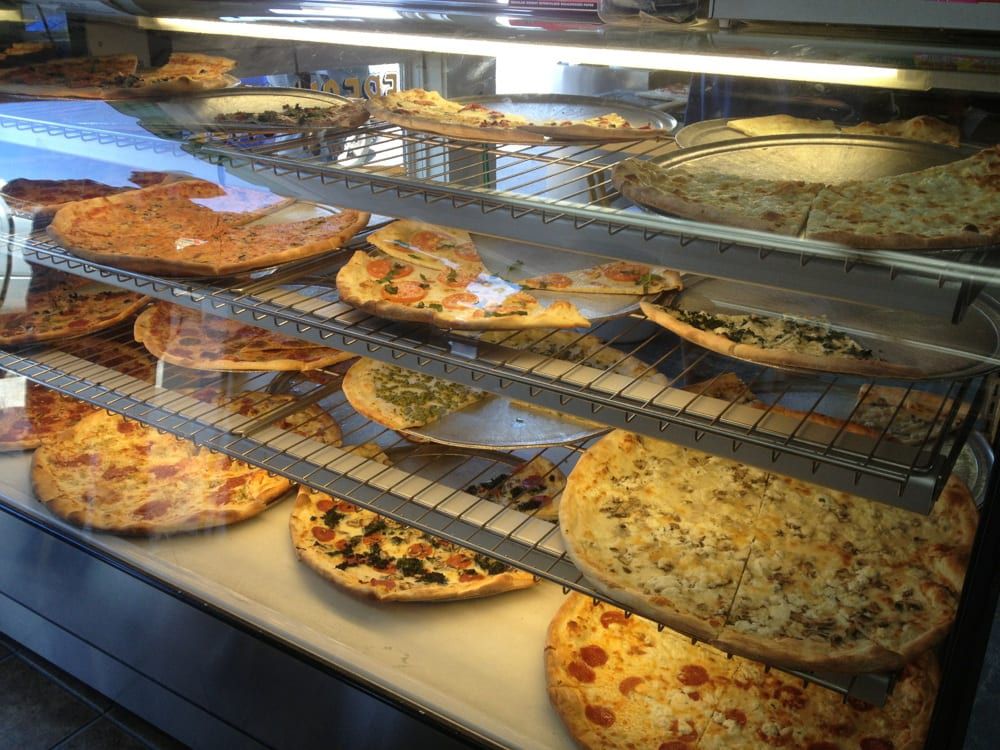 Selection of New York-style pizzas in display case.