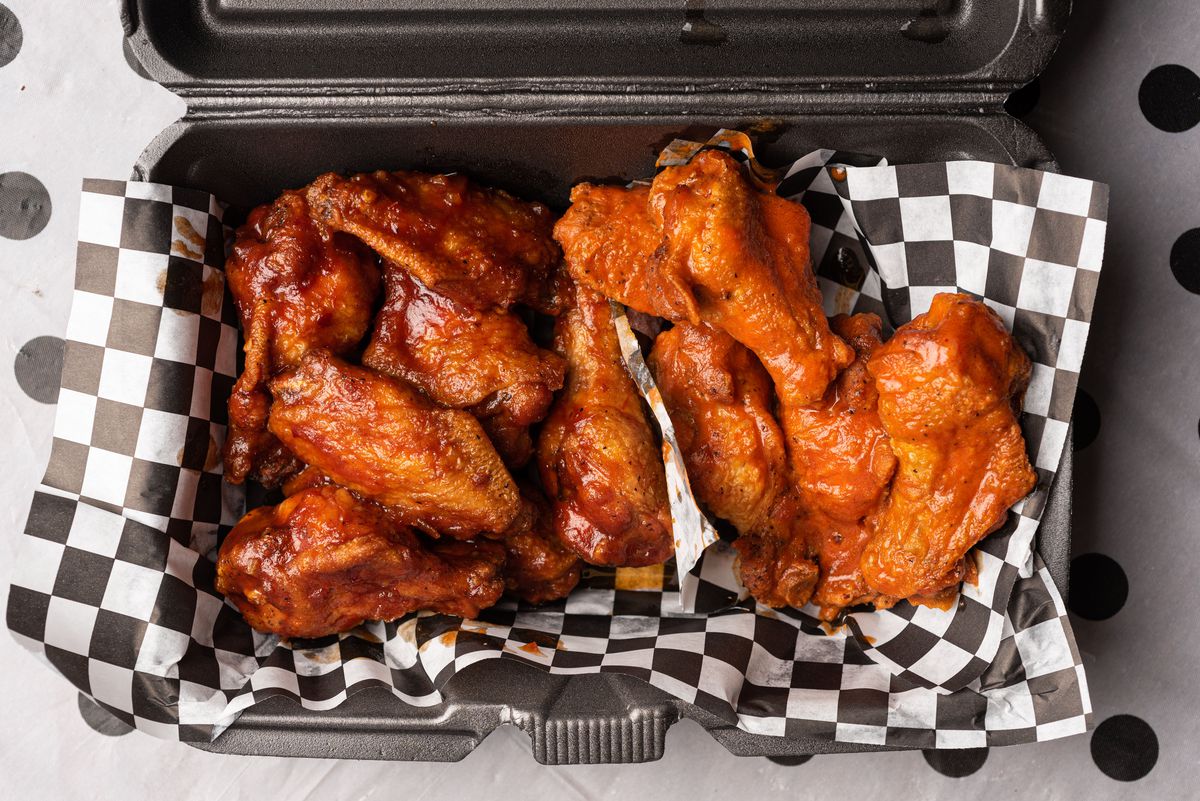 An overhead shot of a black Styrofoam container with wings and sauce inside.