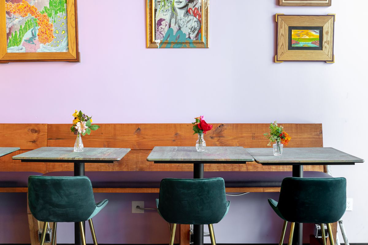 A row of two-top tables against a light pink wall with colorful artwork.