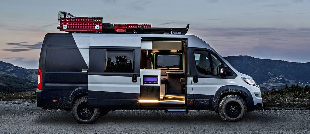 A grey and black camper. The doors are open and the interior has seats and a stereo. There are red storage compartments on the roof of the van.