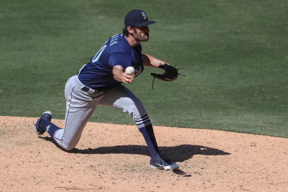 Pitcher in Mariners navy alternate jersey releases a pitch from a shoulder-height sidearm slot.
