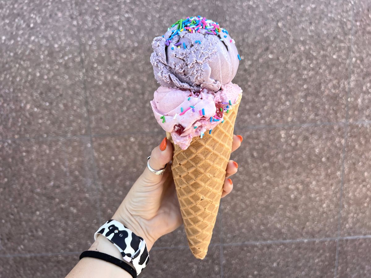 A hand holds a cone of purple ice cream topped with sprinkles