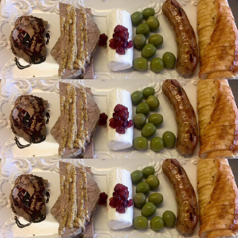 A plate with liver mousse, pate, goat cheese, olives, sausage, and a sliced baguette 