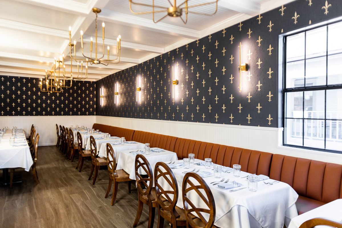 The dining room in Restaurant Beatrice, where the upper half of the wall is lined with navy blue wallpaper emblazoned with gold fleur dis lis.