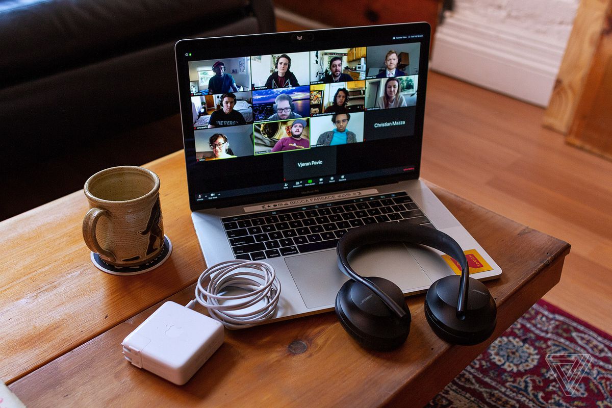 Image of a laptop with Zoom meeting in progress on the screen, on a table with headphones, charging cable, and cup of coffee nearby.