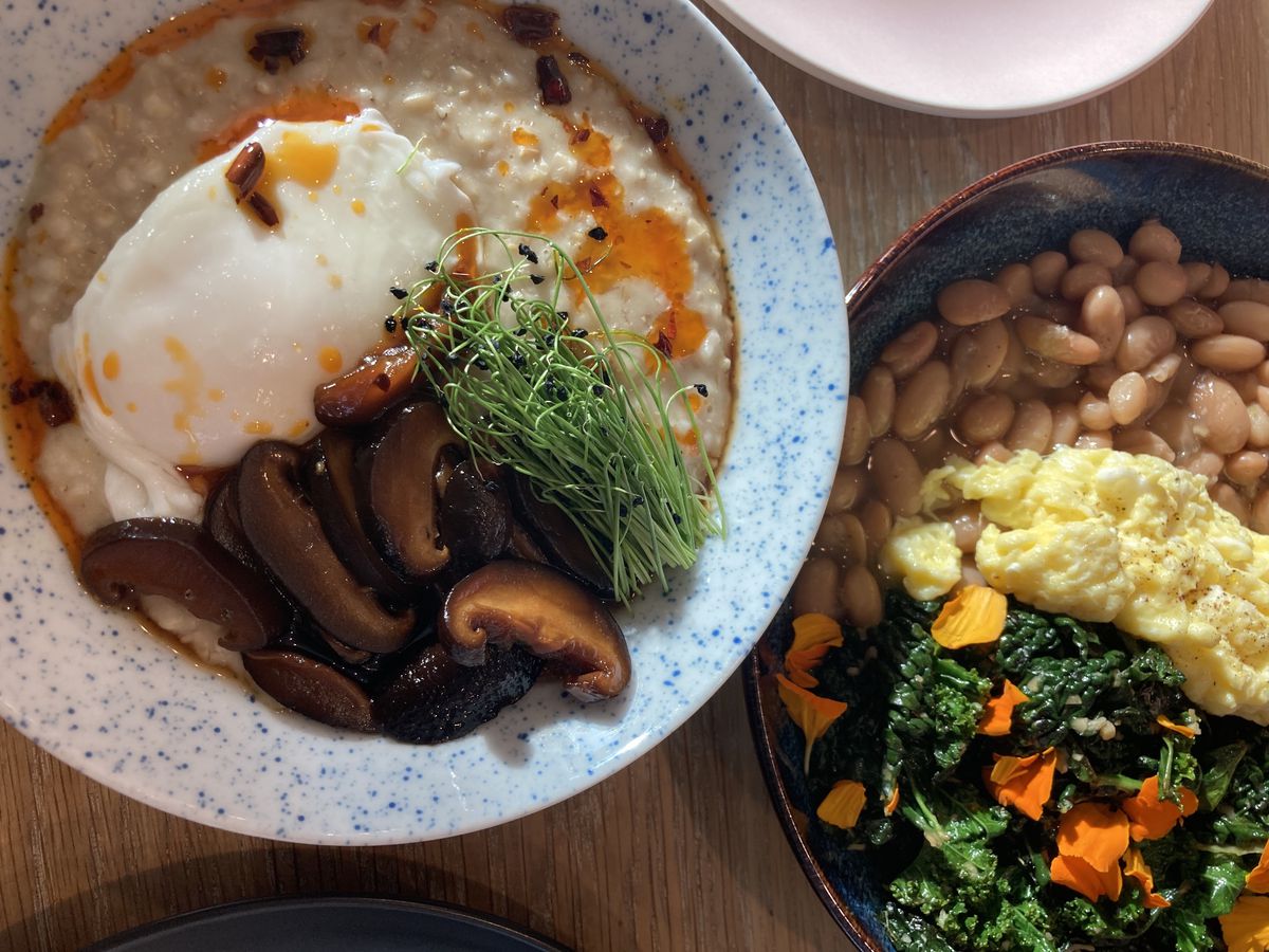 A bowl of poached-egg-topped porridge with mushrooms, as well as a bowl of eggs, beans, and greens at Matutina in Portland.