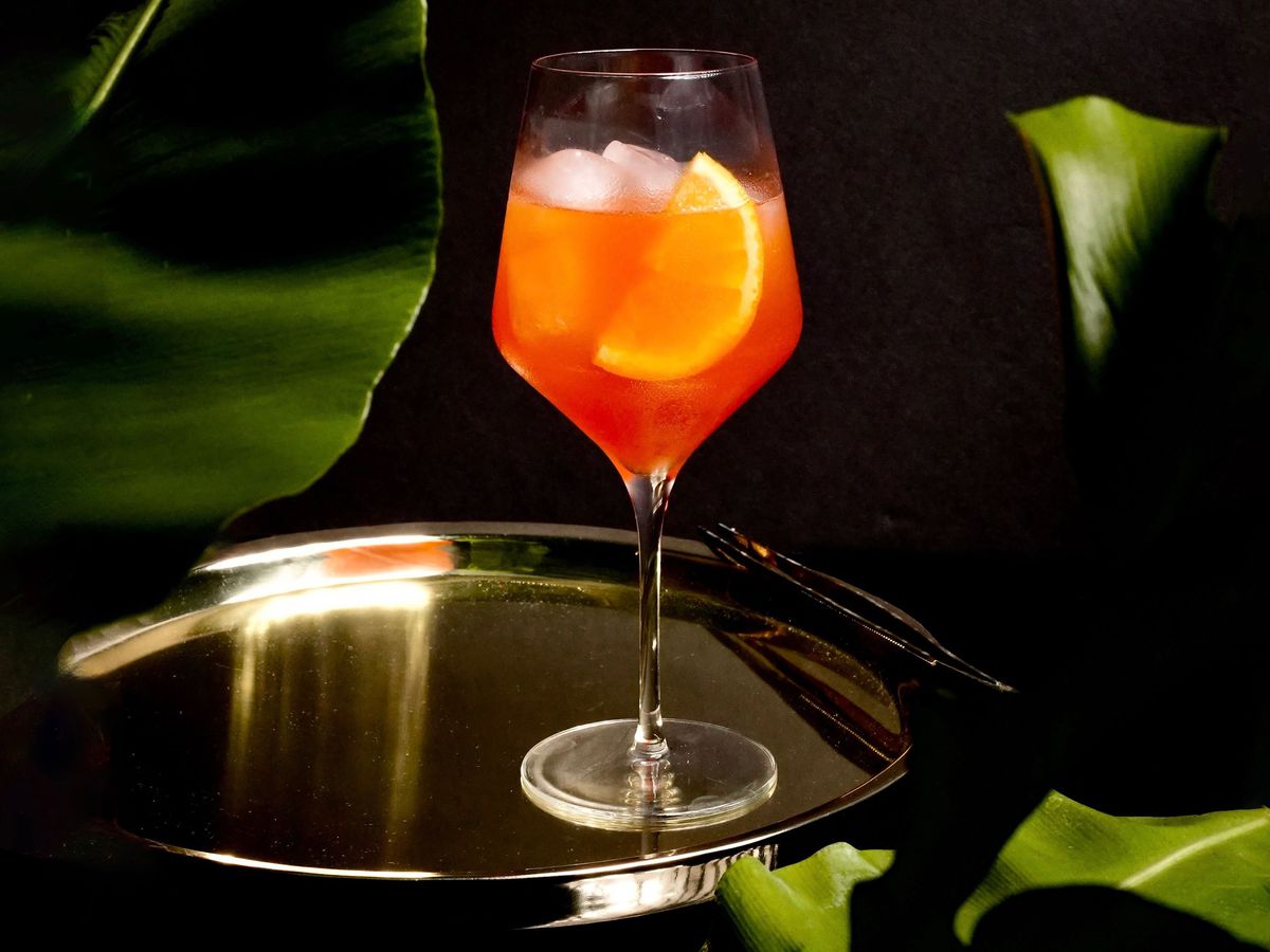 A spritz cocktail in a wine glass on a metal tray.