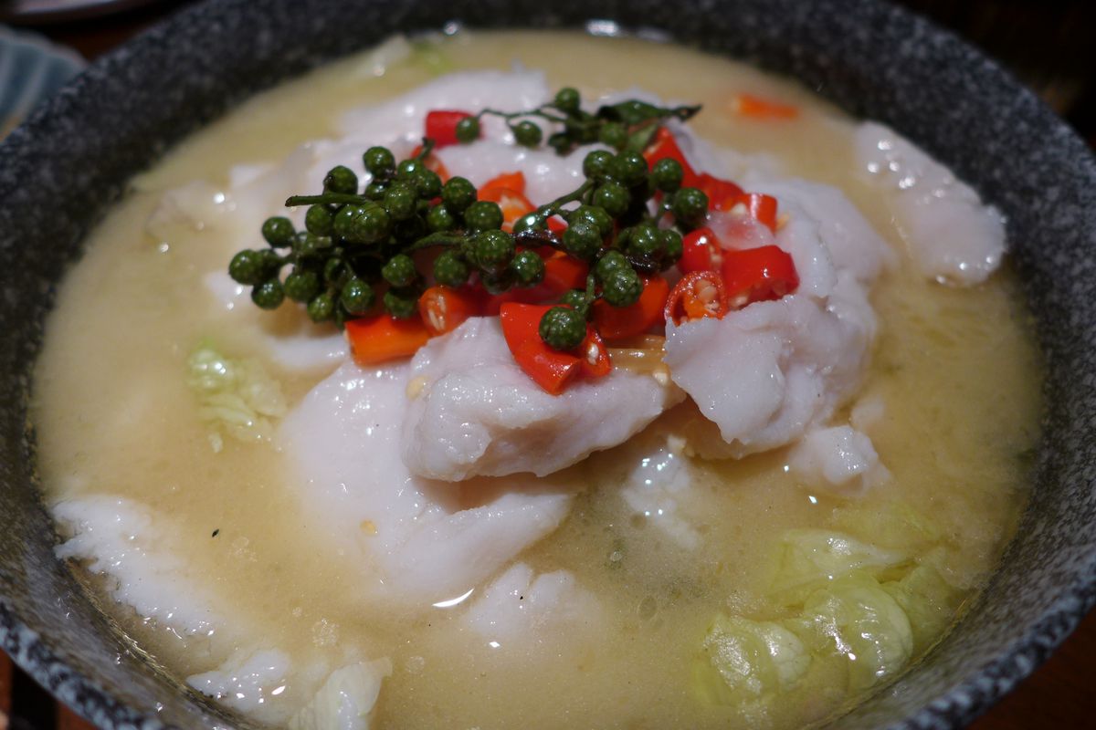 A pale opaque broth with pieces of fish and a tree of green peppercorns on top.