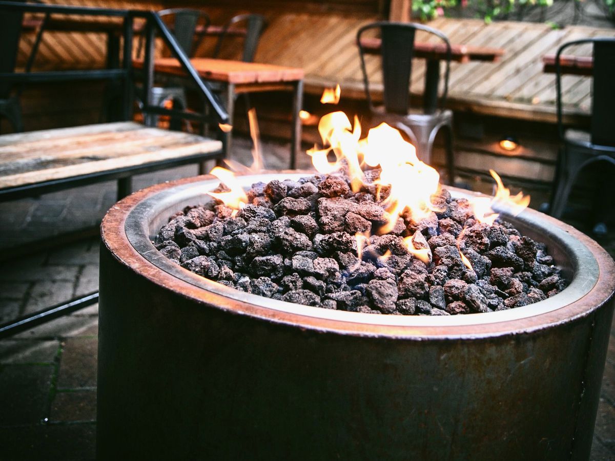 Gas flames leaping from a circular fire pit on a cozy bar patio.