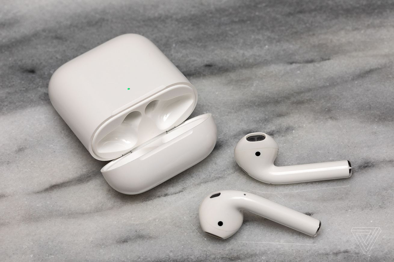 The second-generation AirPods near their charging case on a white surface.