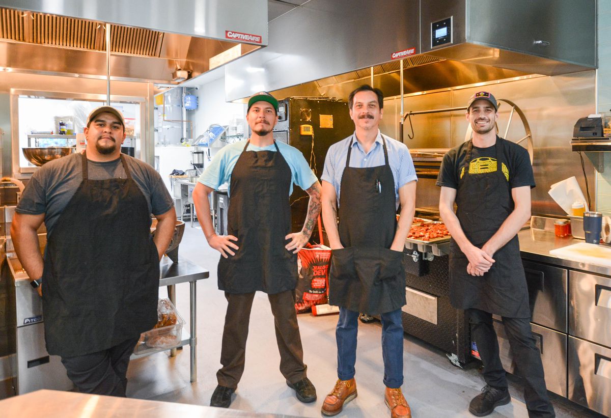 Four men look stern while standing inside a restaurant kitchen in Orange County.
