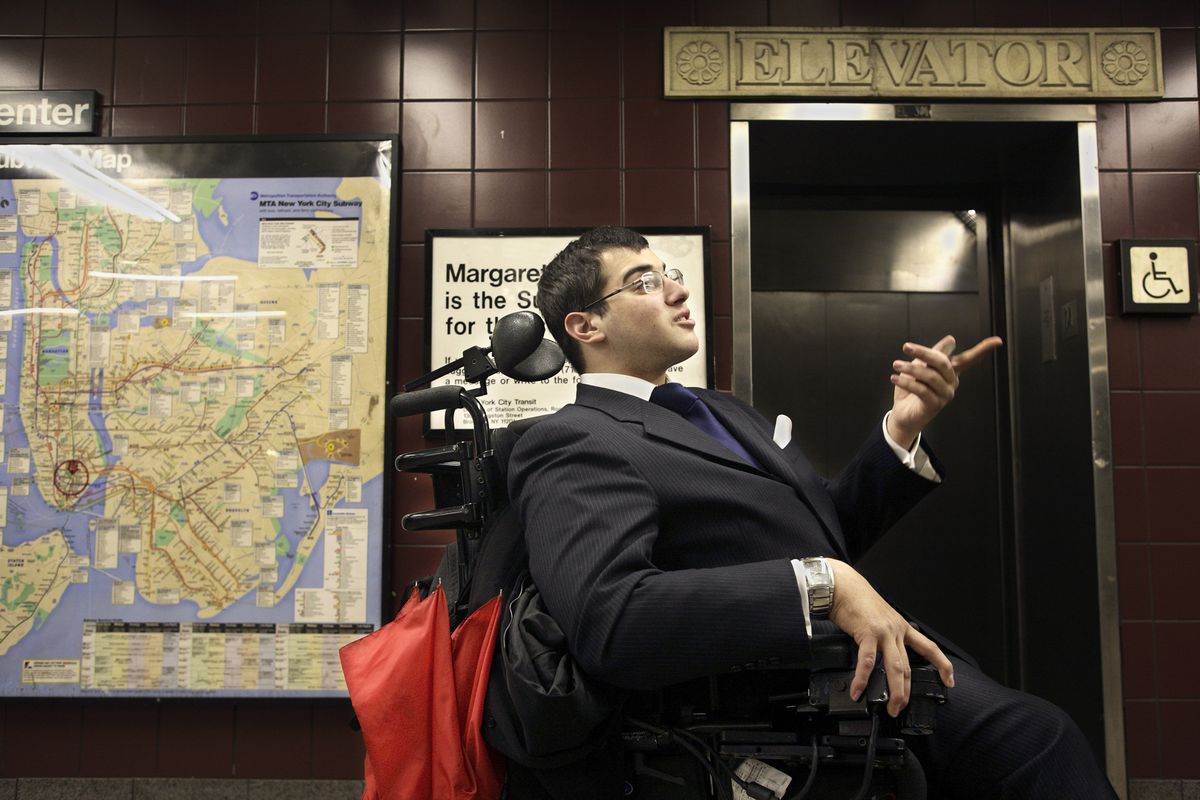 A man wearing a suit in a wheelchair in front of an elevator.