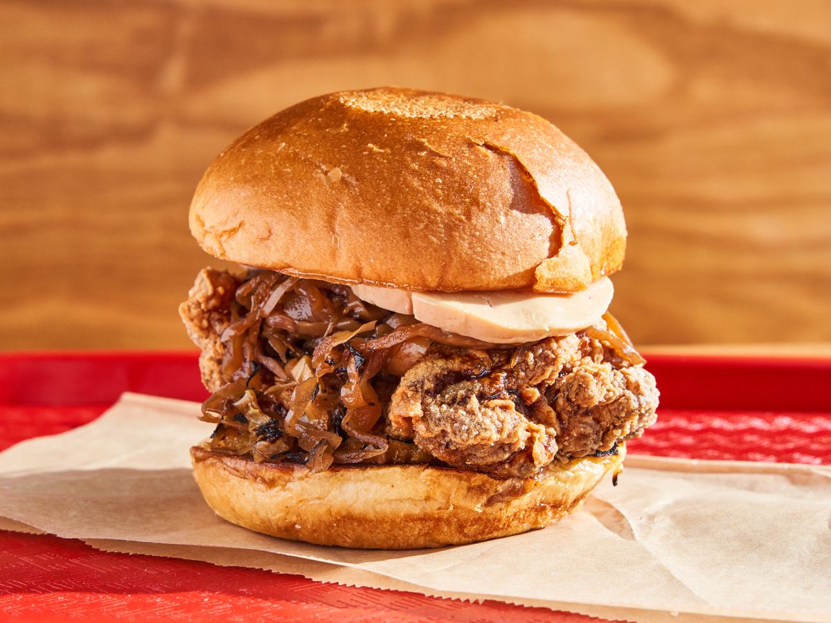 A fried chicken sandwich is stacked on parchment paper on a red cafeteria tray.