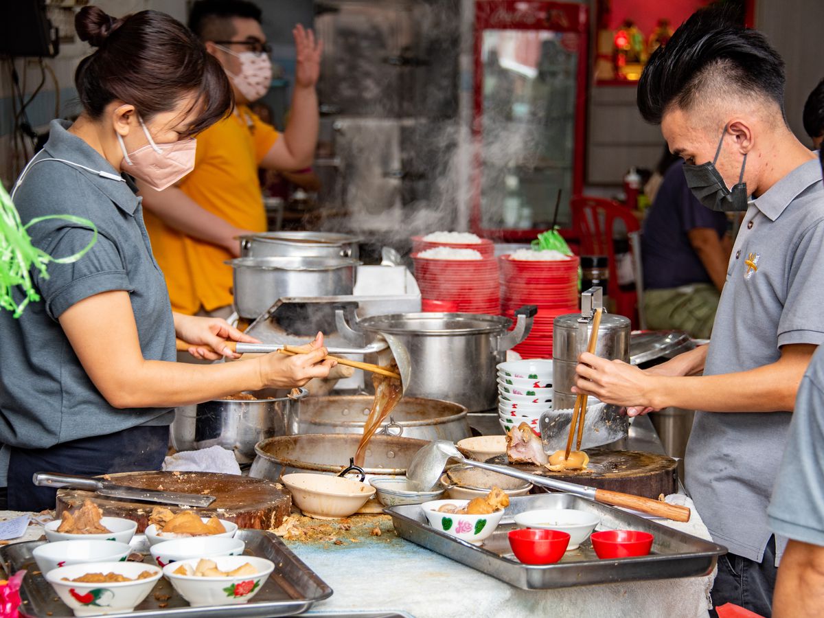 Chefs stand on both sides of a kitchen counter preparing bak kut teh