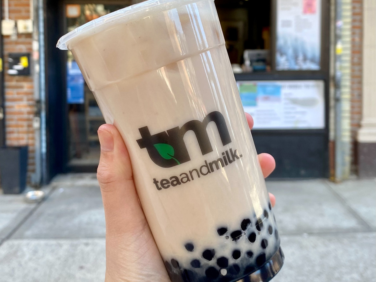 A hand holds up a brown bubble tea with boba.