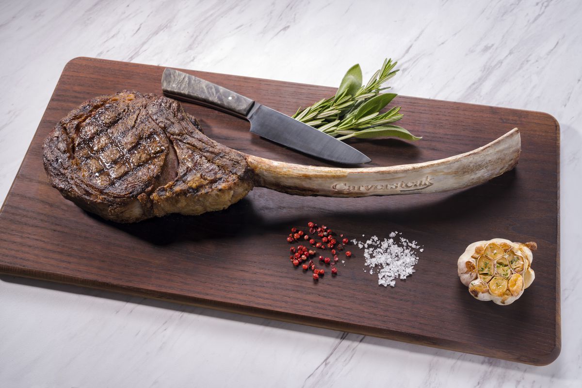 A large steak on a cutting board with a chef’s knife.