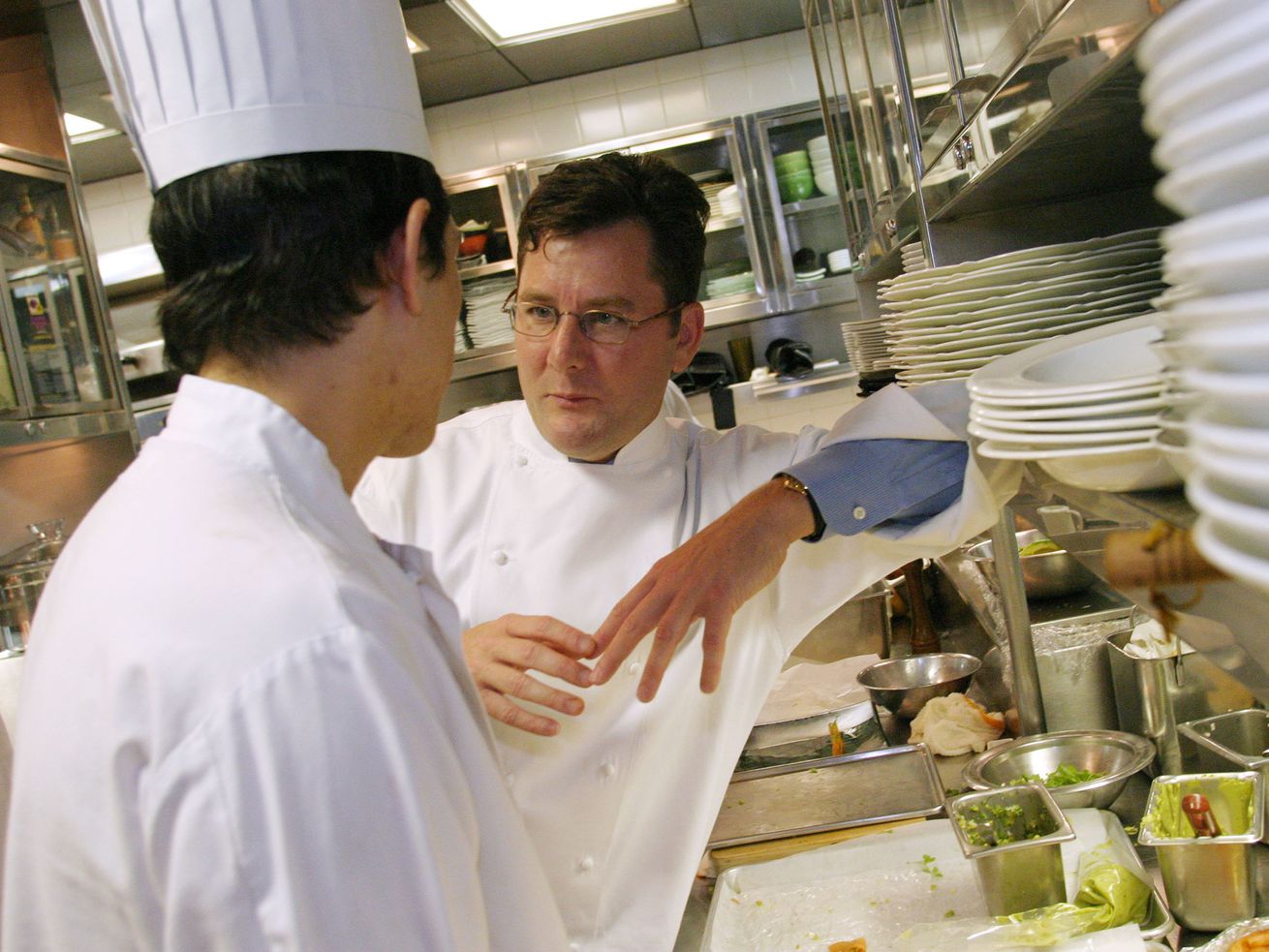 A man in chef’s whites talks to another chef in a restaurant kitchen
