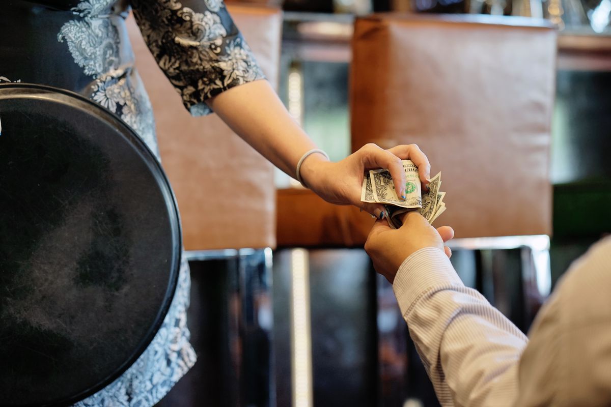 The hand of the waitress takes the tip. The waiter girl receives a tip from the client at the hotel bar. A bartender woman is happy to receive a tip at work. The concept of service