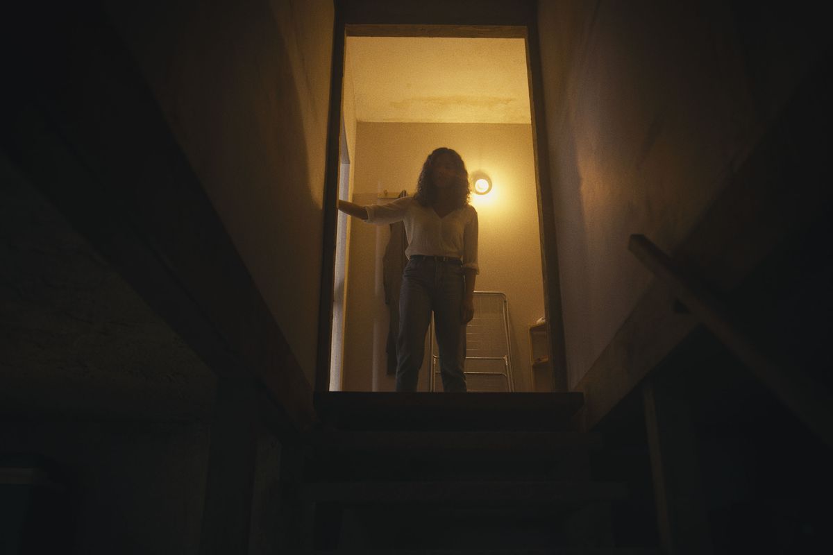 Tess stands atop a staircase leading to a dark basement in the horror movie Barbarian.