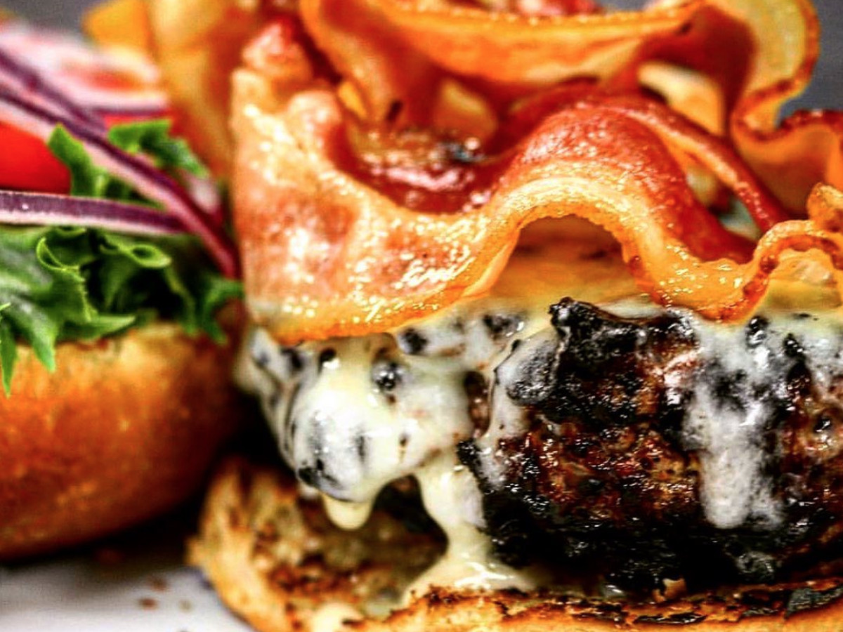A thick piece of crispy bacon sits on top of a cheese-covered beef patty on a toasted bun.
