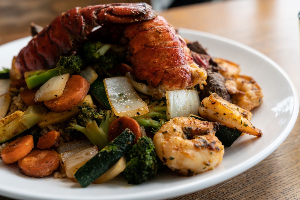 A lobster and shrimp stir-fry with mixed vegetables, including sauteed carrots, broccoli, and onion.