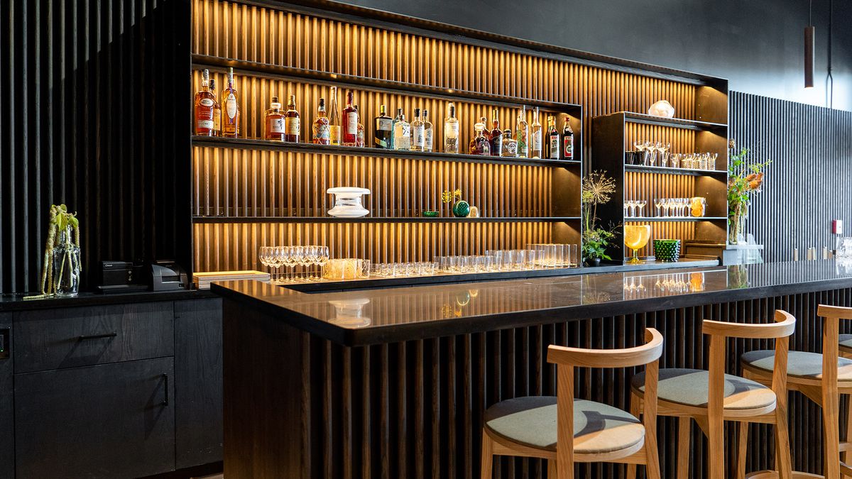 The bar at Tomo, lined with bottles and glasses, with orange accent lighting and dark paint on the walls.
