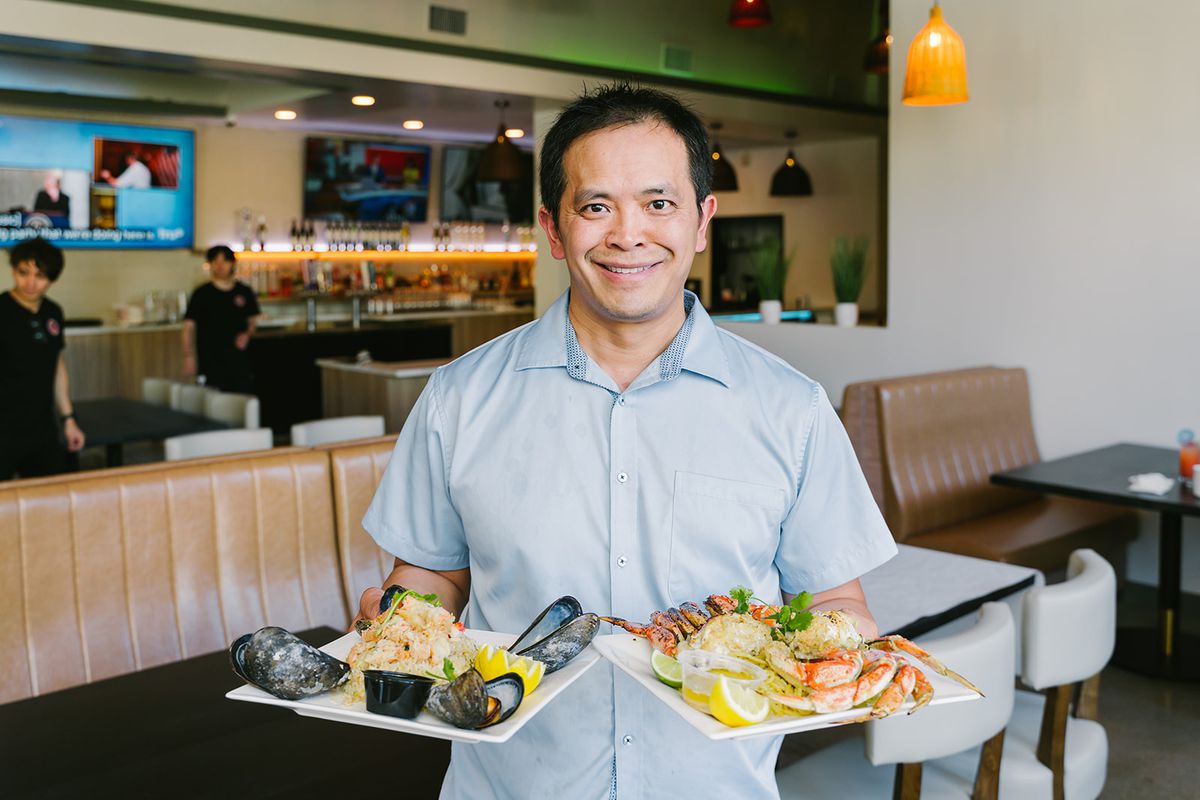 Owner Ryan Mai holding two plates of seafood in Nauti Crab.