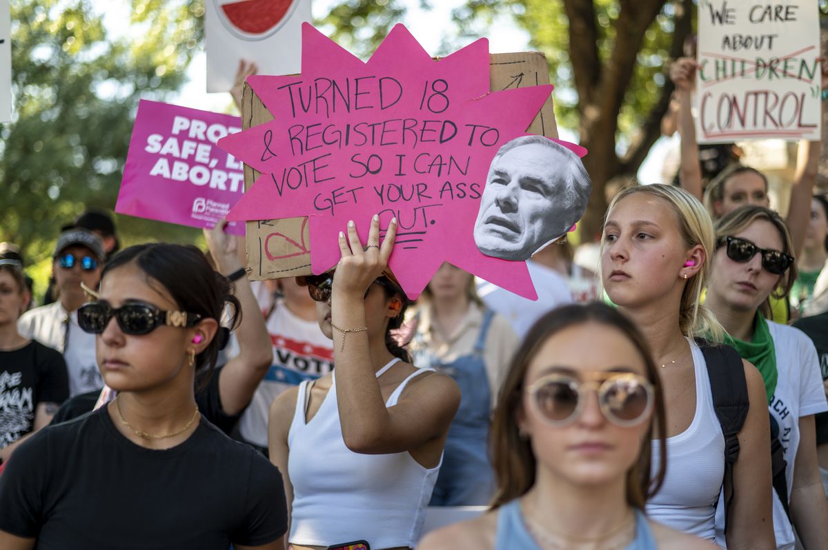A protester holds up a sign threatening to vote Texas Gov. Greg Abbott out of office during an abortion rights rally in Austin on June 25. The sign reads, “Turned 18 and registered to vote so I can get your ass out” alongside a photo of Abbott’s face.