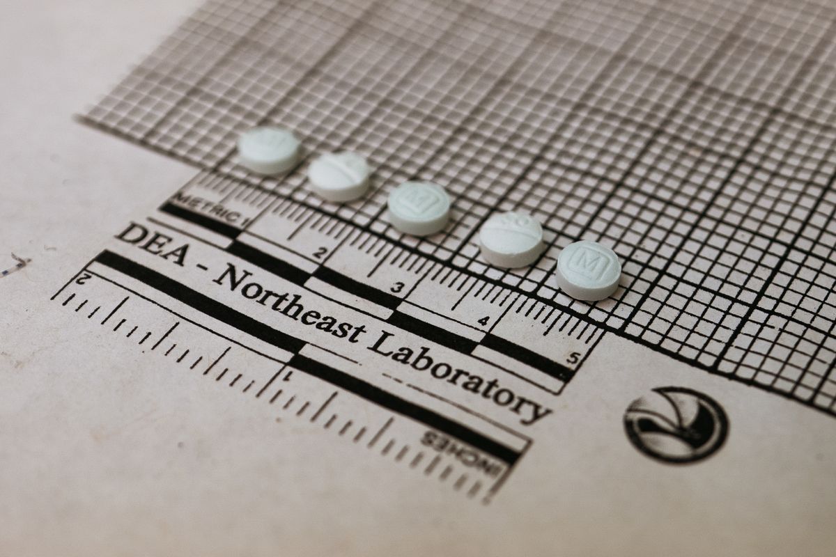 Five small round pills lined up atop graph paper that reads, “DEA - Northeast Laboratory.”
