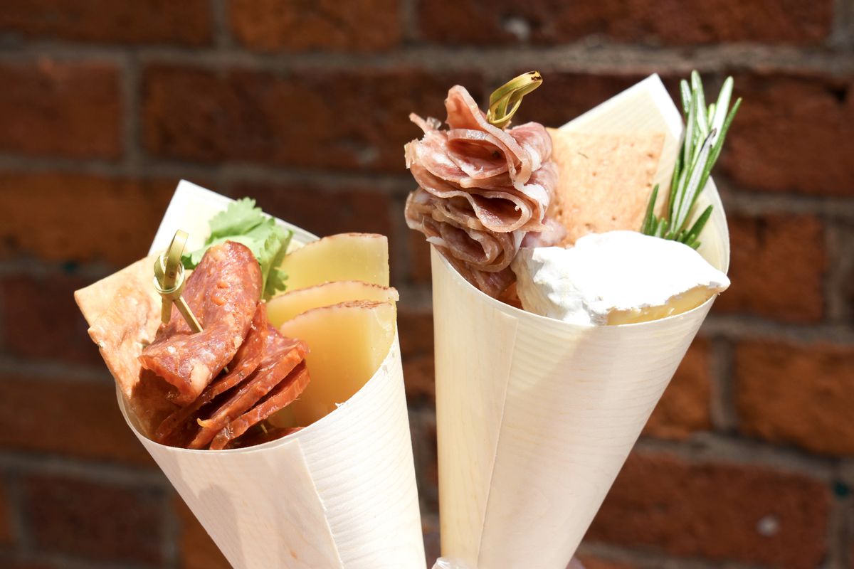 Two beige paper cones filled with meat, cheese, and sprigs of fresh herbs.