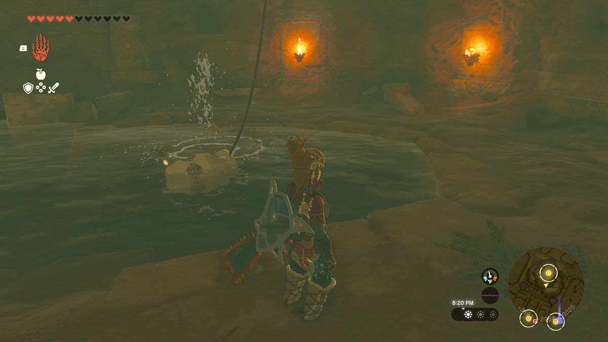 Link stands next to the water source of a well in Tears of the Kingdom. The well is lit up and has a vase and rope used to scoop water out hanging from the top