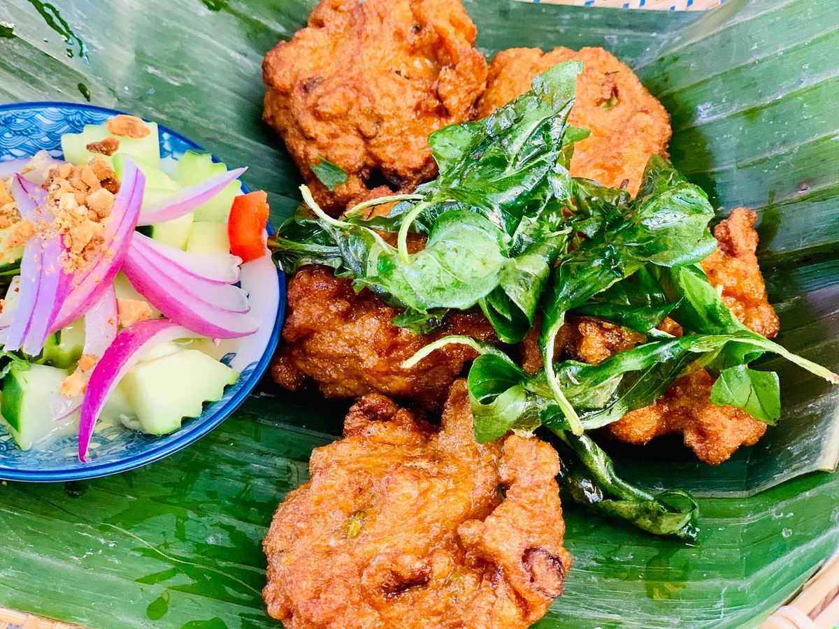 Brown crispy fish cakes with a blue dish of sliced vegetables all in a banana leaf