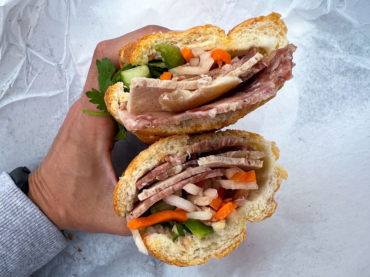 From above, the midsection of a sliced banh mi stuffed with meats and vegetables.