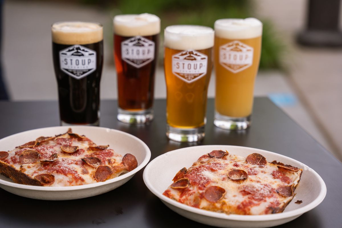 A view of four pint glasses full of beer next to two plates with square slices of pepperoni pizza
