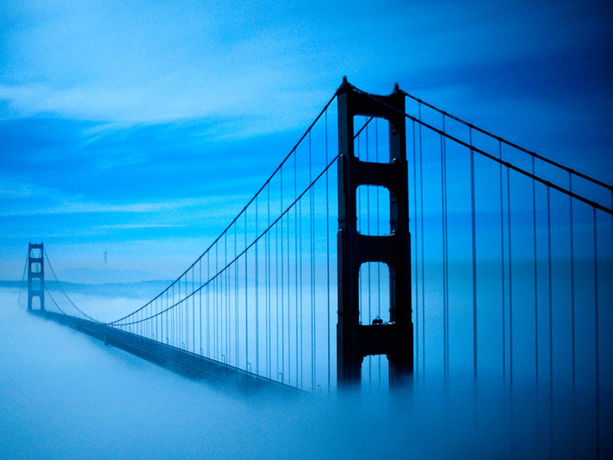 The towers of a suspension bridge, surrounded by eerie bluish fog at night.