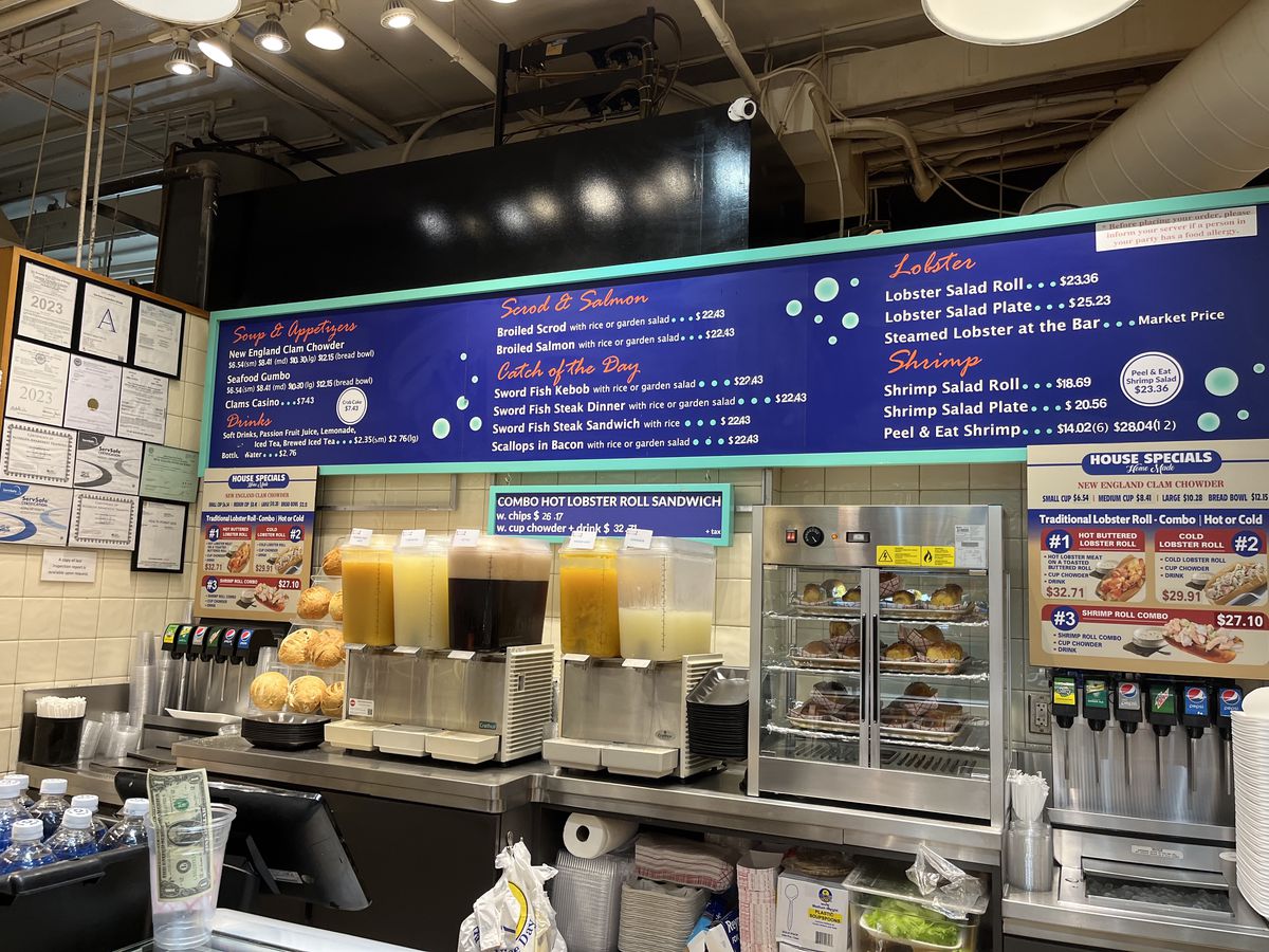 A large blue and white menu listing out different seafood dishes for sale that spans the length of the stall.