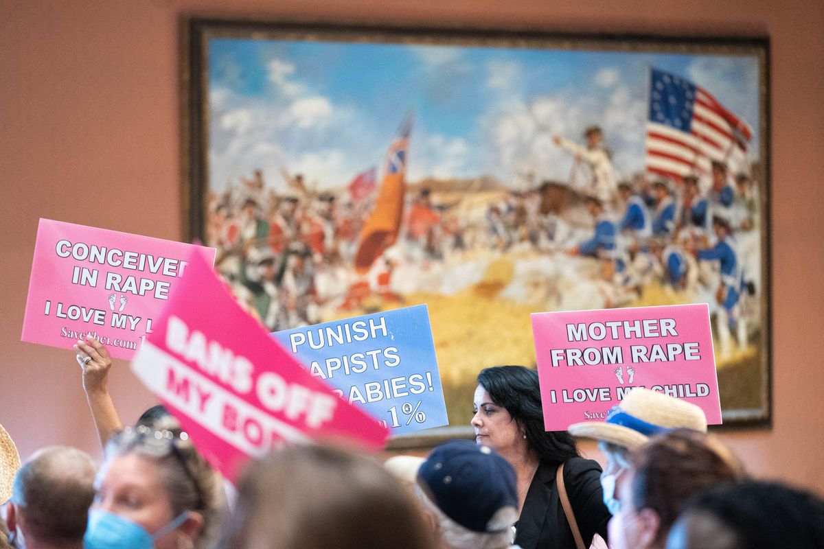 Protesters hold signs with varied slogans related to abortion inside the South Carolina statehouse, in a hallway as they pass a large painting of a Civil War battle.