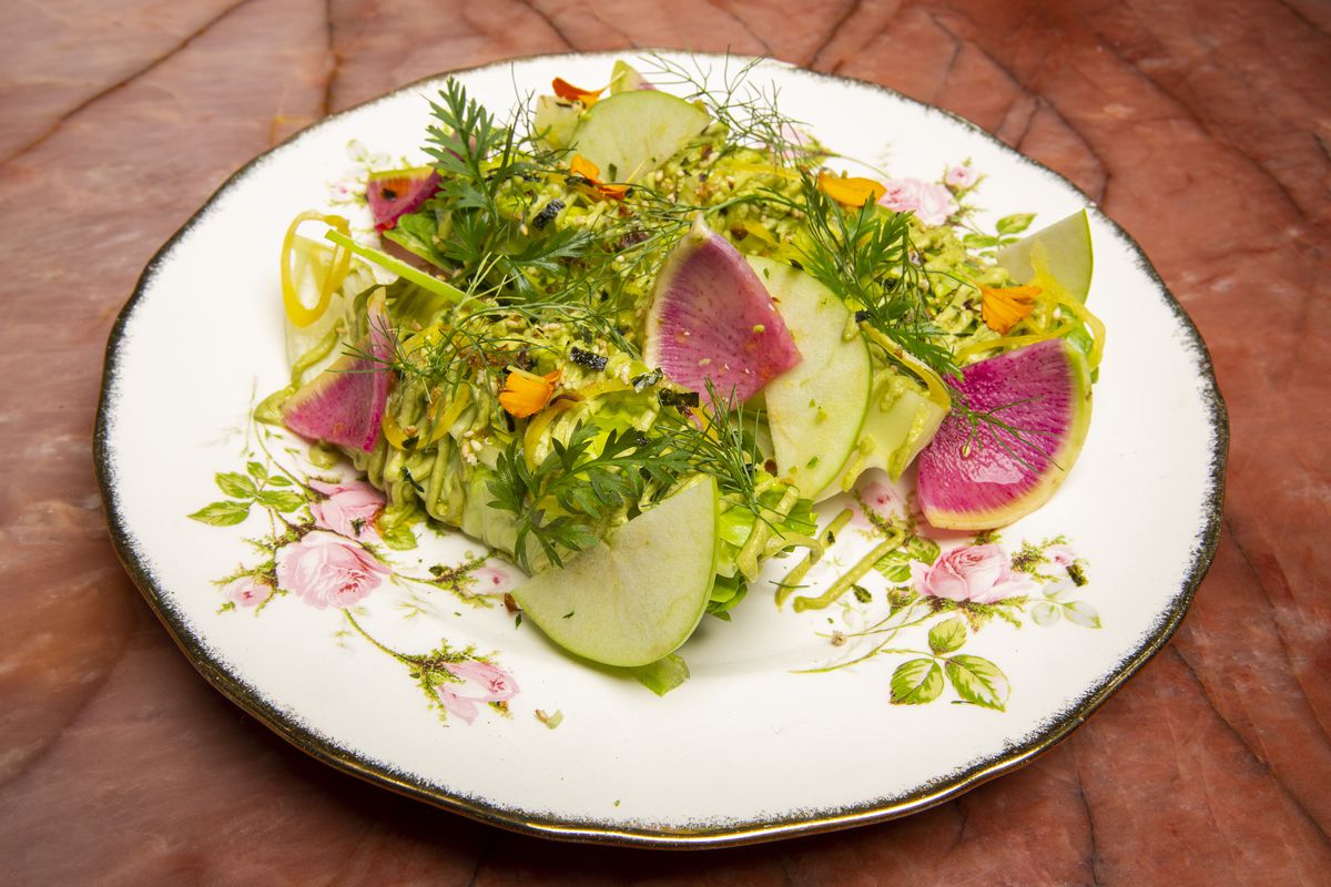 A small green and pink salad on a round plate.