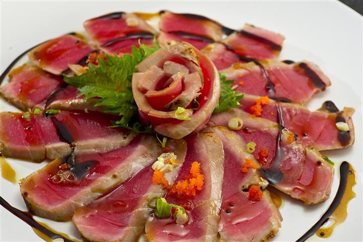 A plate of tuna sashimi arranged in a flower shape with a rosette at the center made from tuna. 